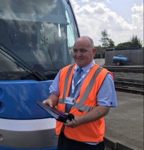 Image of man who works for West Midlands Metro in high vis standing in front of a tram