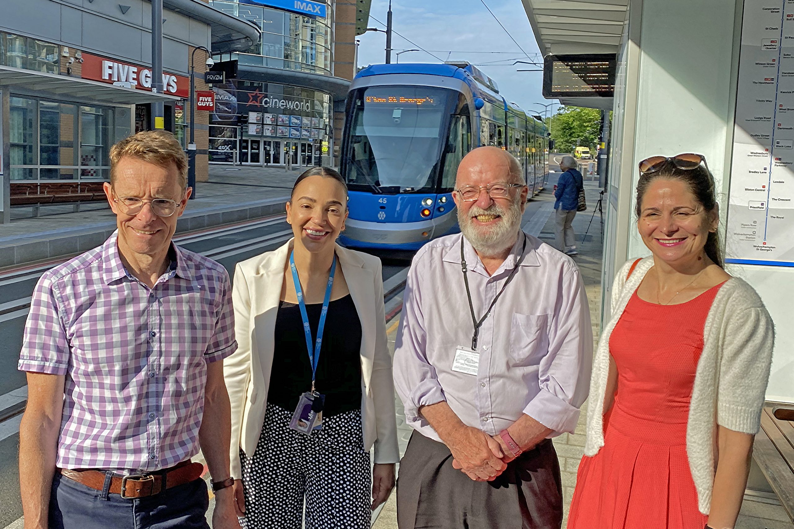 Image of two men and two women smiling in front of a West Midlands Metro tram